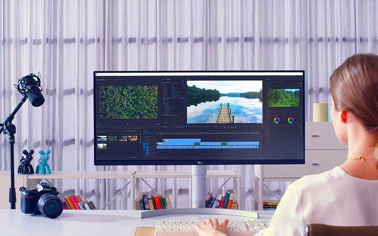 A woman sits at an ergonomic workstation with an ultrawide monitor.