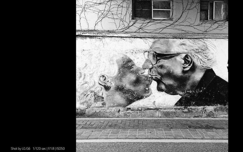 A photography of graffiti of a kissing couple on the street shot by lg g6