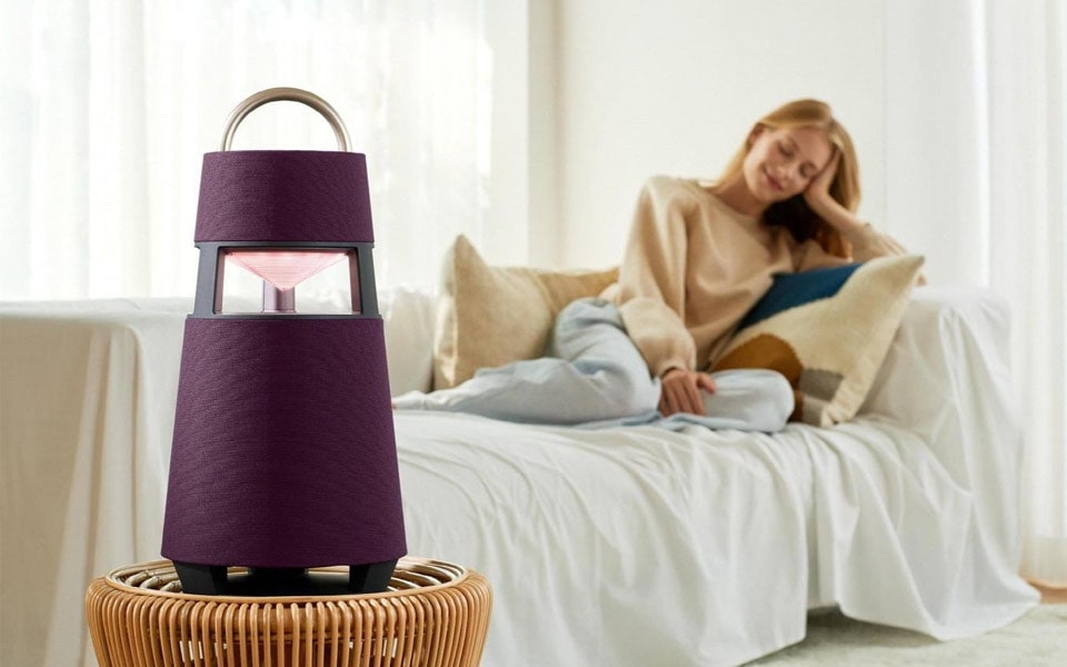 A woman relaxes on the couch while listening to her LG XBOOM360 omnidirectional Bluetooth speaker