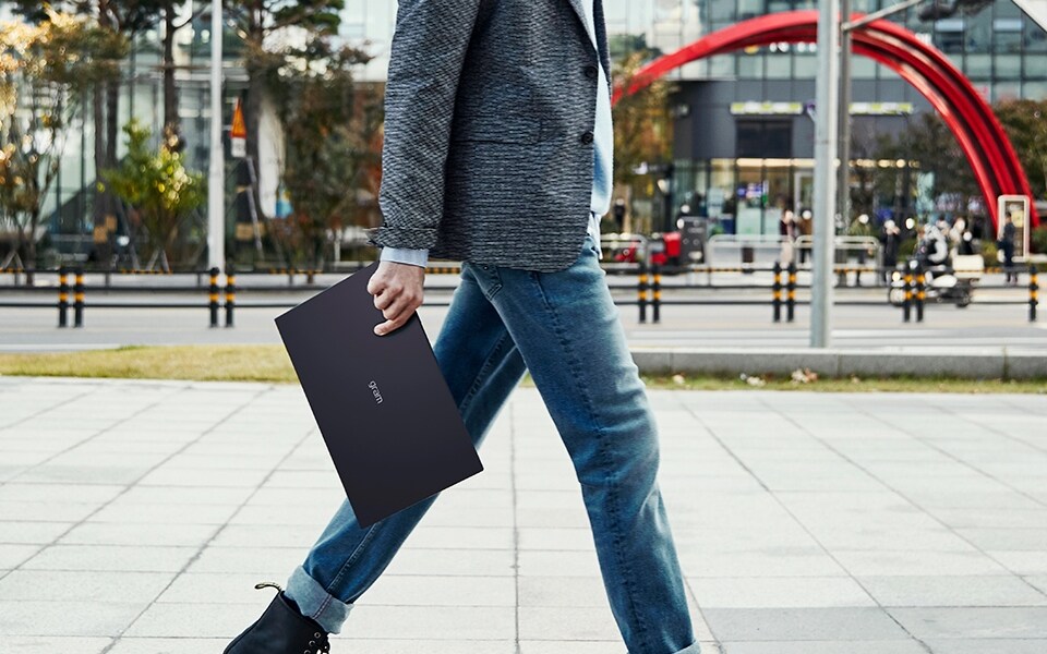 A man is walking outside easily holding a laptop in one hand