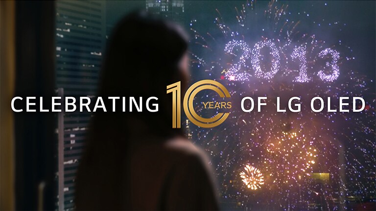 A woman watches a firework display from her window with a cluster that writes out 2013. The overlay text reads, "Celebrating 10 Years of LG OLED."
