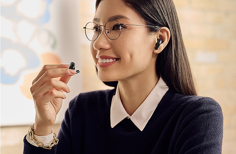 A woman is using the earbuds and holding one in her right hand while whispering into it.