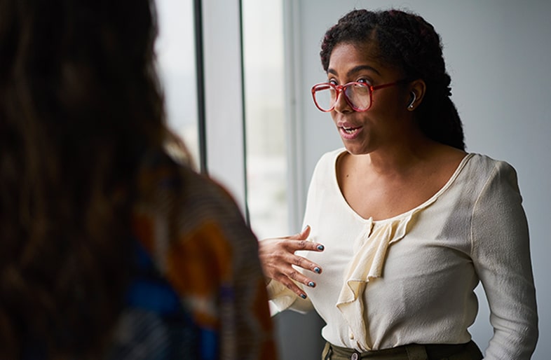 Two women are talking. The woman facing out is wearing the earbuds.