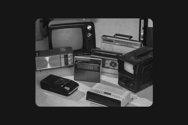 A black and white photograph showcasing a collection of vintage electronic appliances arranged together, including an old CRT television, several portable transistor radios, a cassette tape recorder, and a boombox from the late 20th century.