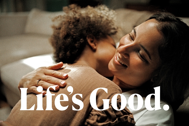 A smiling woman embracing a child indoors, with the text "Life's Good." overlaid at the bottom.