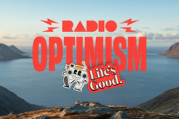 A promotional graphic with a scenic background of mountains and ocean. Bold red text reads "RADIO OPTIMISM" with lightning bolt icons on either side of "RADIO." Below the text is an illustration of a small white robot character holding a microphone, next to a red speech bubble containing the white text "Life's Good."