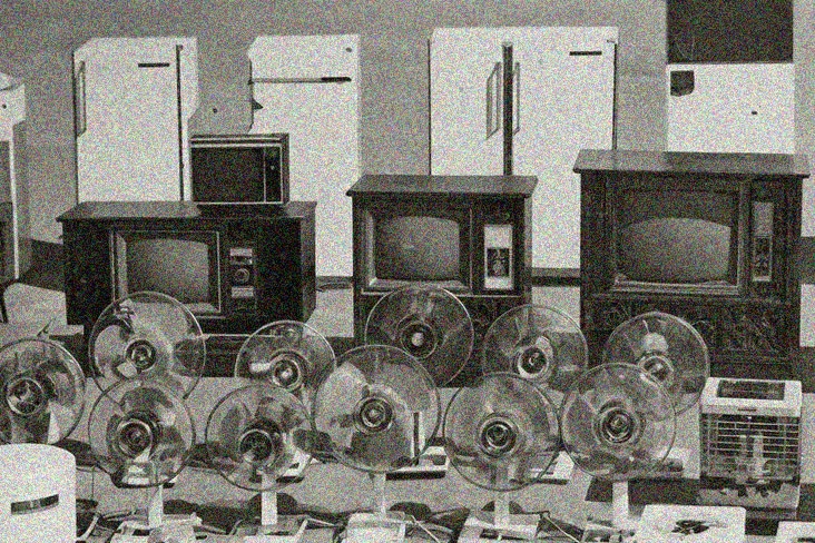 A vintage black and white photograph showing a display of home appliances arranged in rows. In the back row are several white refrigerators of various sizes. The middle row features wooden cabinet-style television sets with round CRT screens. The front row displays multiple electric fans with circular cage guards. An air conditioner unit is visible on the right side.