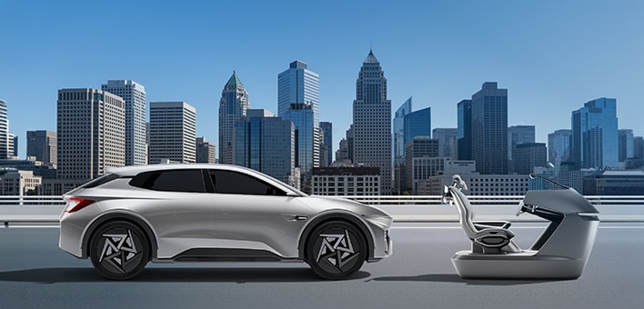 A silver electric SUV concept car parked on a rooftop next to a robotic autonomous charging station, with a modern city skyline in the background.