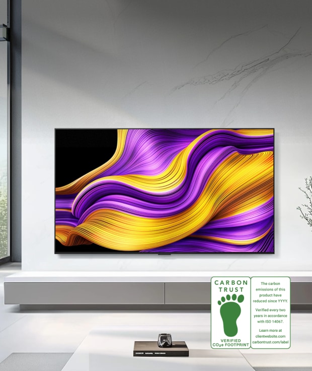LG OLED evo TV mounted on a living room wall with a Carbon Trust certification logo in the bottom right corner.