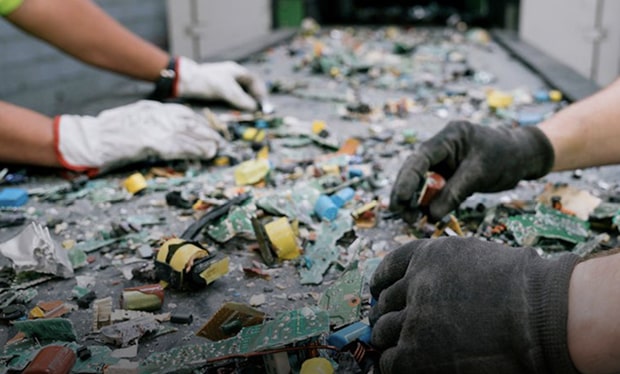 A scene of workers wearing gloves sorting and separating electronic components and discarded materials on a conveyor belt, showing a dismantling and sorting process for recycling and resource circulation