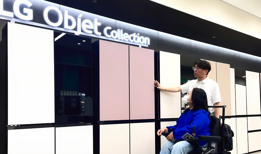 LG store staff assisting a wheelchair user in front of LG Objet Collection refrigerators