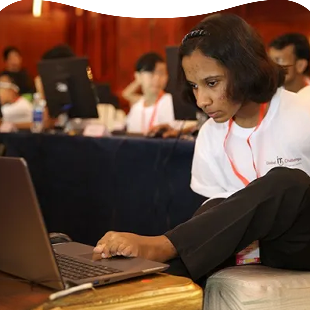 A young participant with a disability focuses intently on completing an IT challenge on a laptop at the Global IT Challenge for Youth with Disabilities (GITC)