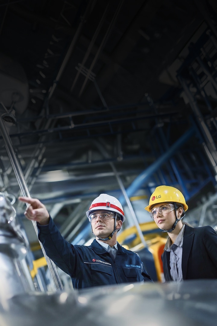Two workers wearing hard hats and safety glasses pointing at and inspecting industrial equipment