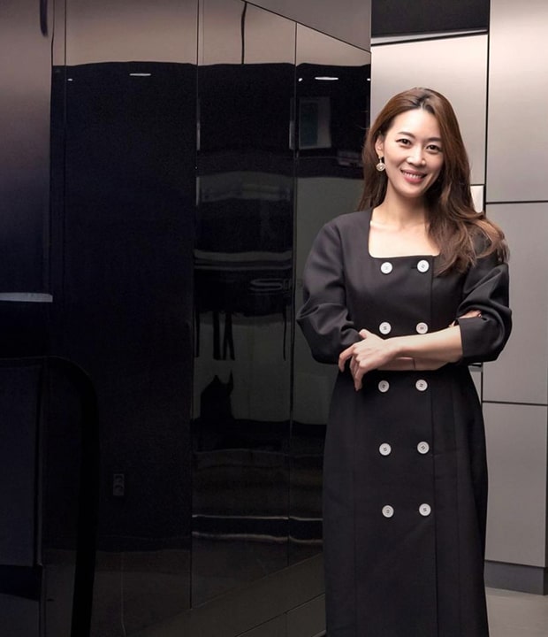 A woman standing and smiling in front of a modern black built-in kitchen