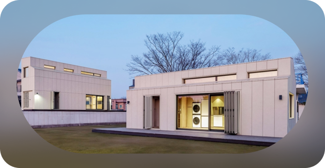 The exterior of the LG Smart Cottage, a modern smart home set on a lawn, with large glass windows revealing an interior space equipped with a washer and dryer.