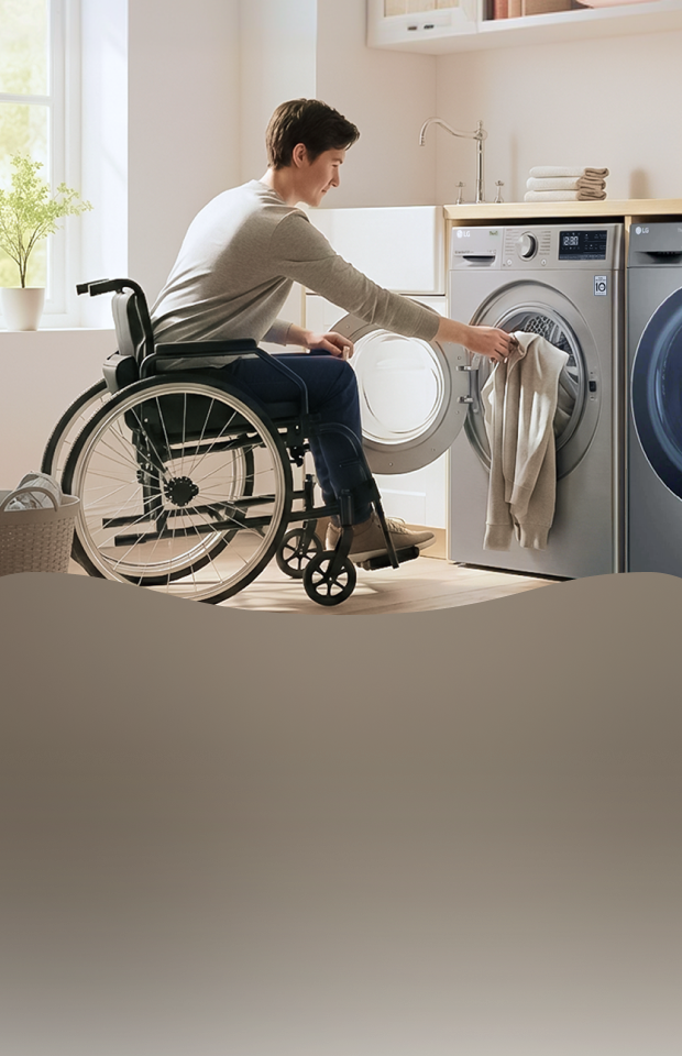 A person using a wheelchair loads laundry into a front-loading washing machine in a laundry room, with a dryer positioned beside it.
