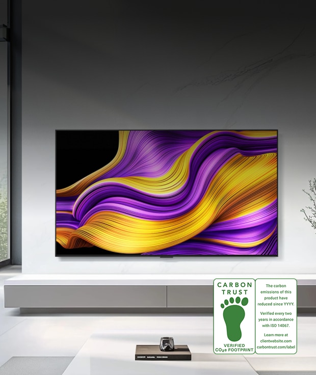 An image of an LG OLED TV product. An LG OLED TV displays an abstract graphic with purple and yellow wave patterns on screen. In the lower right, a CARBON TRUST VERIFIED CO₂e FOOTPRINT certification mark is shown along with the text: 'The carbon emissions of this product have reduced since YYYY. Verified every two years in accordance with ISO 14067. Learn more at carbontrust.com/label.'
