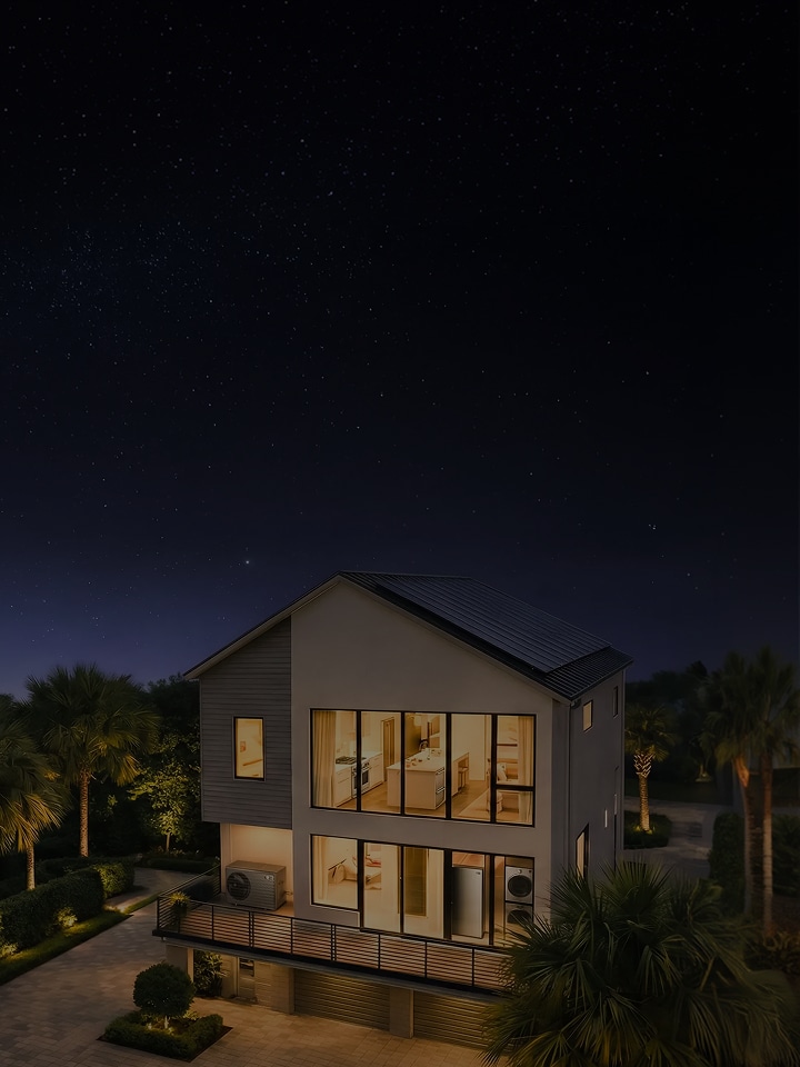 A panoramic view of a two-story house illuminated under the night sky. An outdoor air conditioning unit is installed on the terrace, and various home appliances such as a refrigerator, washing machine, and dryer are visible inside the house through large glass windows.