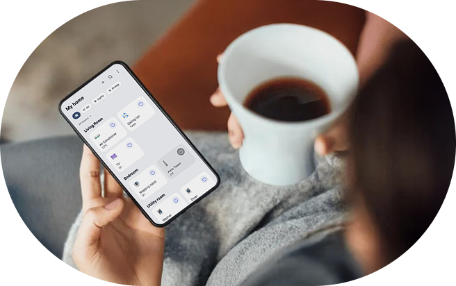 An image of the LG Smart Home app. A person sitting on a sofa drinking coffee operates the app on a smartphone. The app screen shows the 'Multi Home' view, listing smart devices such as air purifiers, lights, and air conditioners by room — living room, bedroom, etc. — along with their status.