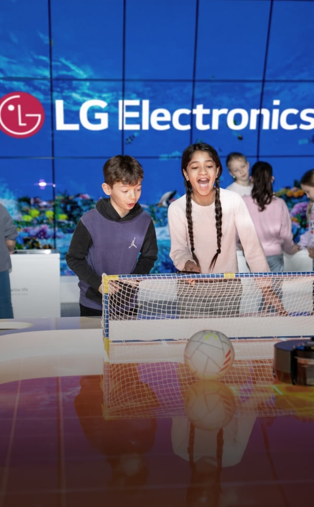 Children participating in an interactive activity with a small soccer goal and ball in front of a large LED wall displaying the LG Electronics logo.