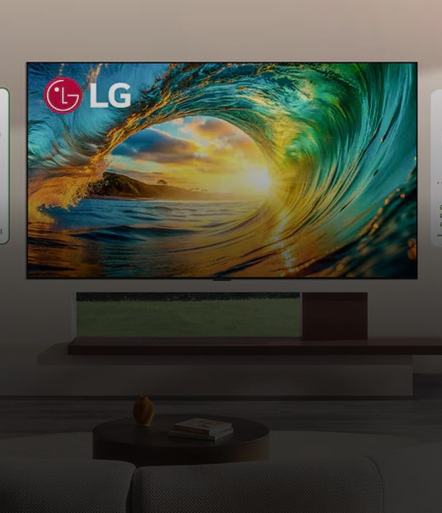 An promotional image showcasing a large LG television mounted on a wall in a modern living room setting, surrounded by environmental certification labels. The TV screen displays a vibrant, colorful image of a large ocean wave cresting under a bright golden sunset, with the LG logo in the top left corner of the screen. The TV sits above a long, minimalist wooden media console. In the foreground, part of a light-colored sofa with a green pillow and a round coffee table are visible.