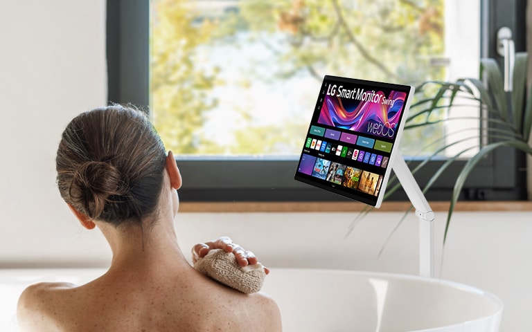 A woman looks at an LG 360 monitor while taking a bath.
