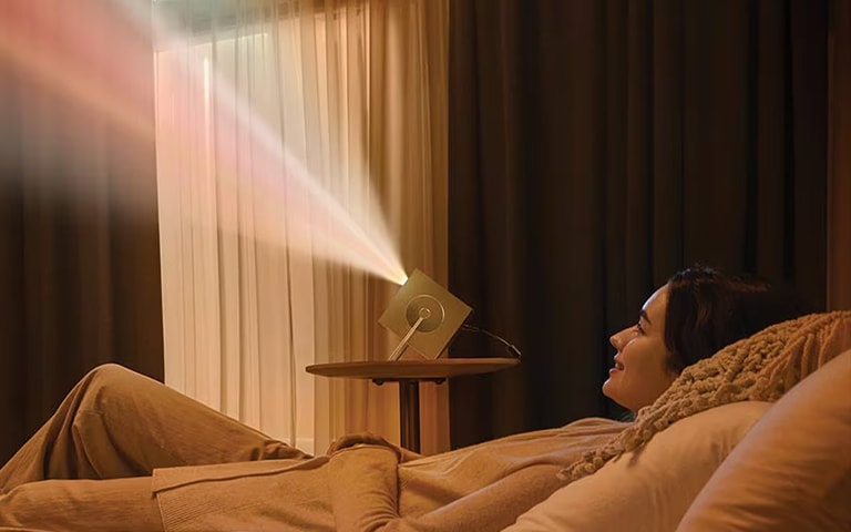A woman lying down and watching a video projected on an LG 4K projector