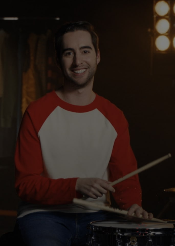 Josh Harmon covering his ears in front of a drum set under lighting.