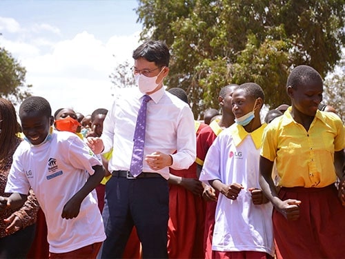 A male LG employee wearing a white shirt and a tie is standing in front of children.