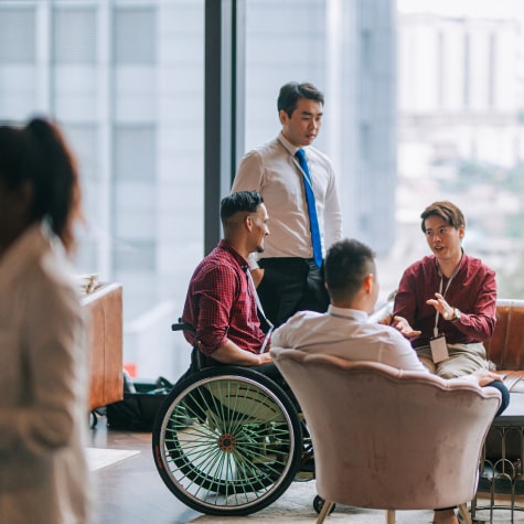 Two people sitting in a wheelchair and two sitting people gather together.