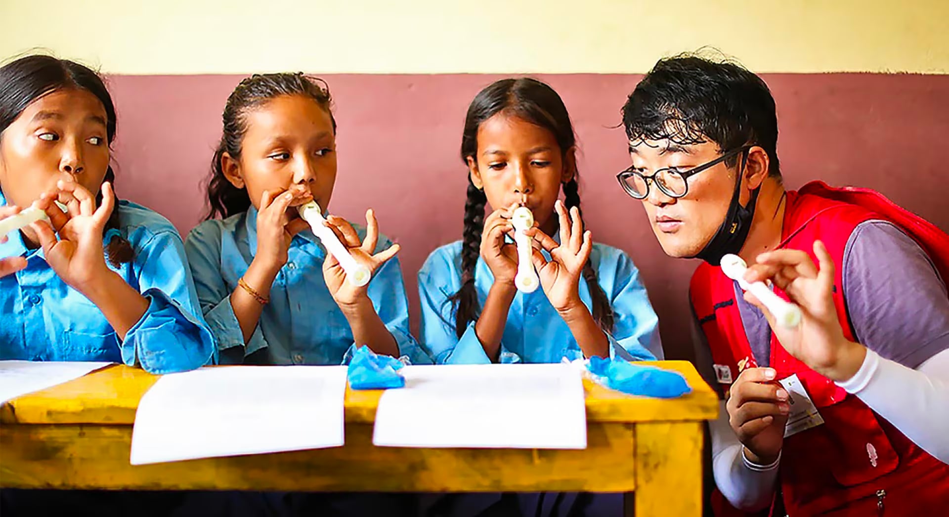 LG volunteers in a red vest tell us how to play the recorder to three children.