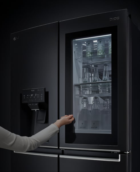 A woman is peering inside the LG Dios refrigerator through InstaView.