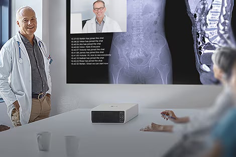 Orvosi személyzet egy konferencián és a képernyőt nézik az LG ProBeam eszközről.