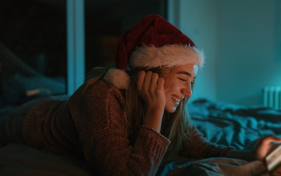 A girl smiling at her smartphone whilst wearing a Christmas hat