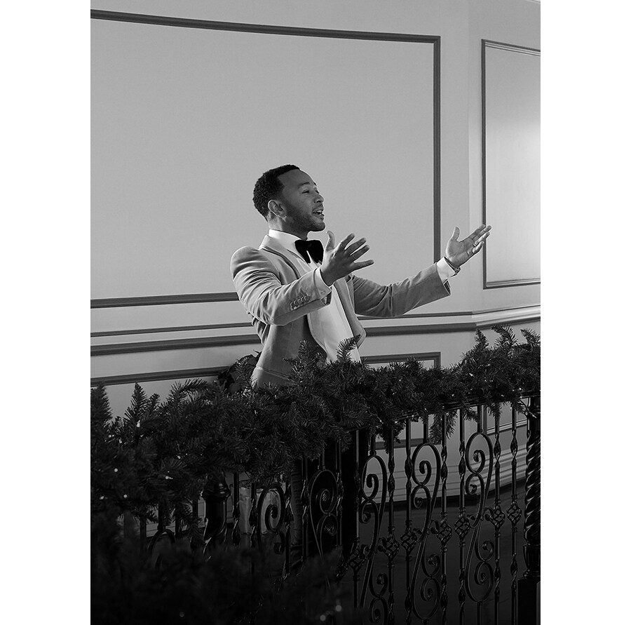 Sångaren John Legend går nerför en trappa och håller i en ledstång dekorerad med juldekoration.