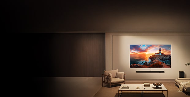Ett modernt vardagsrum med en LG-TV monterad på väggen som visar en färgstark solnedgång. Den högra sidan av rummet är varmt upplyst och möblerad med en beige fåtölj, ett vitt soffbord och en golvkudde, medan den vänstra sidan tonas ut i mörker för att framhäva skärmen.