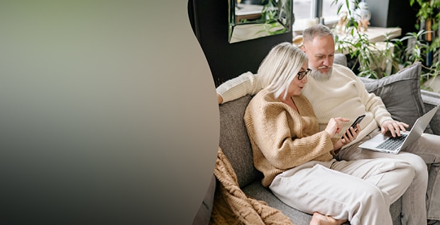 Äldre par som sitter i en soffa hemma och använder en smartphone och en laptop, med LG:s varumärke och sloganen *Lifes Good* samt etthäfte med titeln 'Din handbok i vardagsteknik'