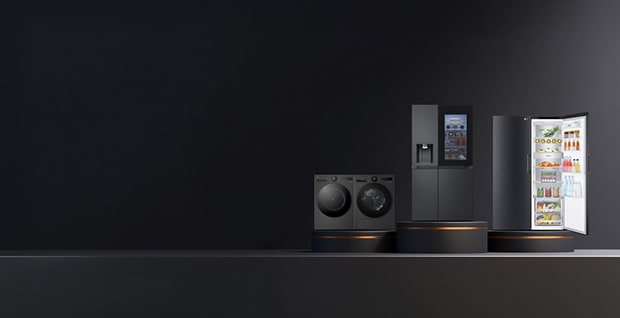Bilden visar en grupp eleganta, svarta **LG-vitvaror** placerade mot en mörk bakgrund. Till vänster syns en stor frontmatad tvättmaskin bredvid en matchande torktumlare. I mitten står ett högt kylskåp, och till höger finns en diskmaskin med öppen lucka där man kan se prydligt placerade korgar och disk inuti. Designen är modern och stilren och framhäver LG:s premiumkänsla.