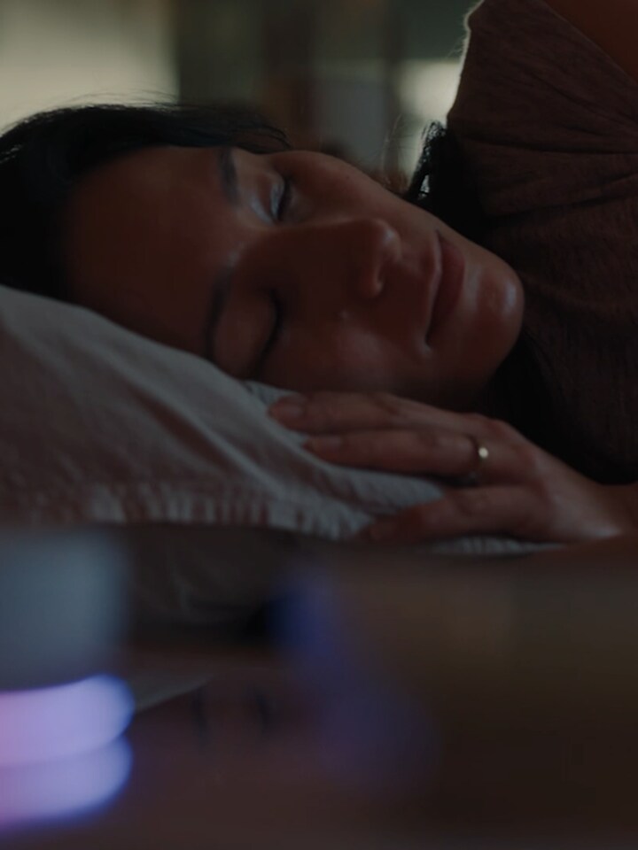 Kvinna som sover med huvudet på kudden, väckarklocka bredvid sängen på nattduksbordet.