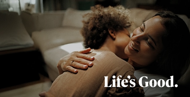 A woman smiling while embracing a young child, with the small text "Life's Good" below.