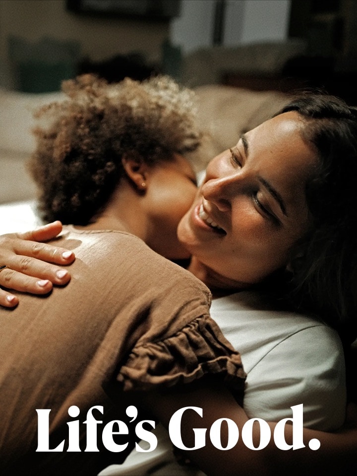 A woman smiling while embracing a young child, with the small text "Life's Good" below.