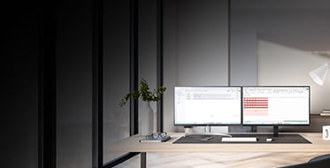 Ett modernt kontor med två datorskärmar på ett skrivbord framför stora fönster. Skärmarna visar kod och ett användargränssnitt. Kontoret är ljust inrett med växter, en skrivbordslampa och en kaffekopp. 