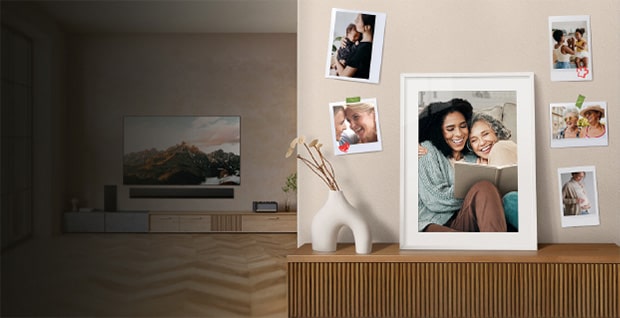 Ett varmt och hemtrevligt vardagsrum i en kampanj för mors dag. Till höger syns inramade familjefoton på väggen och på en möbel, med en stor bild i mitten där två kvinnor sitter nära varandra och ler medan de läser tillsammans. Runt omkring finns mindre spontana bilder av nära och kära som skapar en personlig och känslosam familjekänsla. En vit dekorativ vas står på ett träskåp under bilderna. I den mjukt belysta bakgrunden syns en modern TV med ett bergslandskap på skärmen som förstärker den lugna hemmiljön. Till vänster visas svensk kampanjtext om fri hemleverans och betalning med Klarna, och längst ner till höger syns sloganen “Life’s Good”.