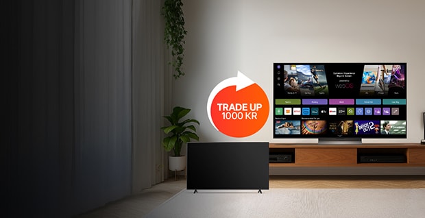 Ett modernt vardagsrum med en LG smart-TV som står på en TV-bänk i trä och visar olika streamingappar på skärmen. En subwoofer står på golvet till vänster. En röd cirkel med texten "BYT UPP TILL LG OLED TV" syns på bilden. Bakgrunden är minimalistisk med neutrala färger och en krukväxt delvis synlig till vänster.