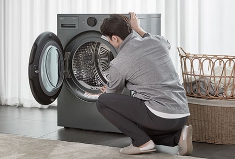 ชายกำลังตรวจสอบเครื่องซักผ้า LG ในห้องซักรีดข้างตะกร้าผ้า สมัครสมาชิก ข่าวสารผลิตภัณฑ์ โปรโมชั่น อัปเดตใหม่ LG.