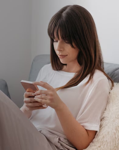Một người phụ nữ đang ngồi trên ghế sofa và nhìn vào chiếc điện thoại của mình.