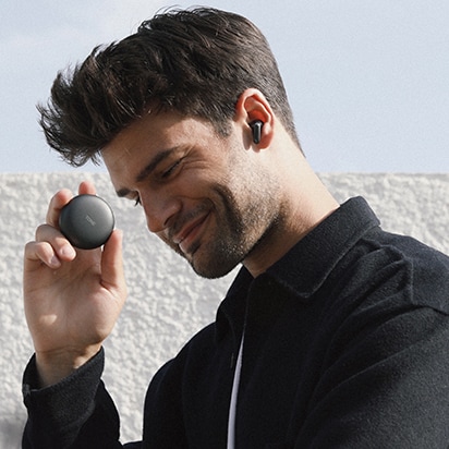 Side view of a smiling man wearing LG TONE Free Black and holding a cradle in his hand