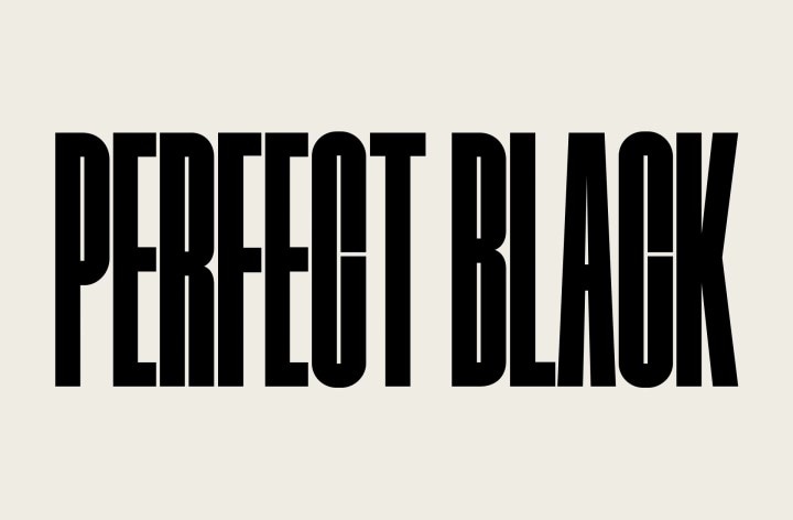 The words "PERFECT BLACK" appear in bold black capitals. A black mountainous scene with crisp definition then rises to cover the letters, also revealing a village and sand dunes. The black copy disappears behind a black sky.