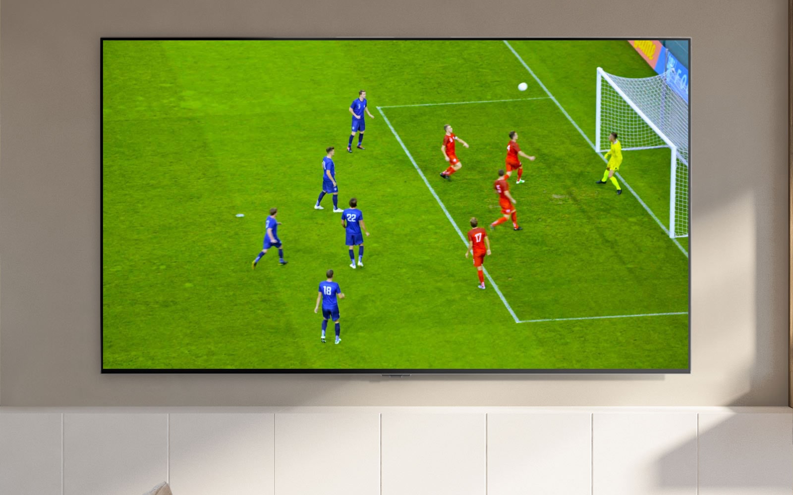 Televizní obrazovka zobrazující fotbalový stadion a hráče, jak dává gól (přehrát video).