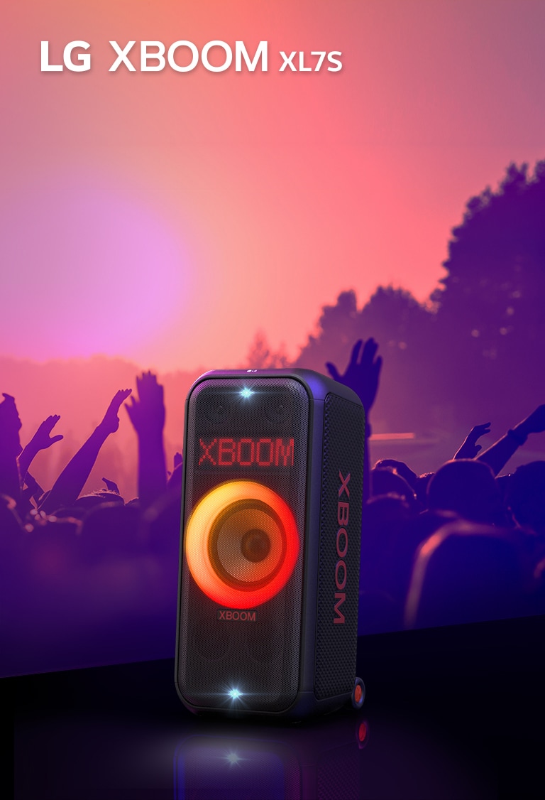 LG XBOOM XL7S je postaven na pódiu se zapnutým červeno-oranžovým gradientním osvětlením. Za pódiem si lidé užívají hudbu.